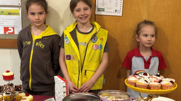 Melody, Cleo and Ophelia standing at a table of laid out with their homemade bakes before the cake sale